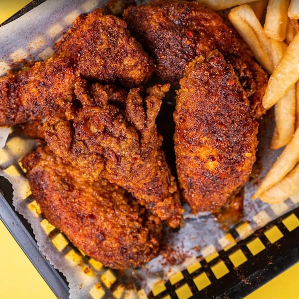 Spicy fried chicken wings and french fries in a black and white checkered basket.