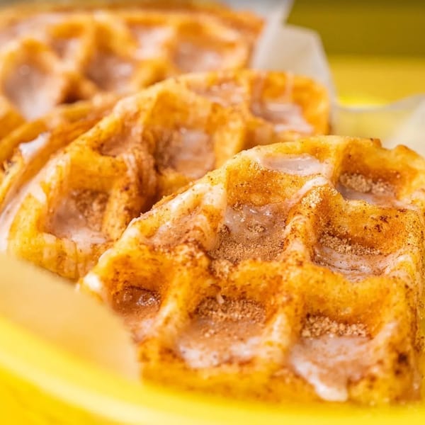 Close-up of golden-brown waffles with white icing and cinnamon sugar, served in a yellow basket.