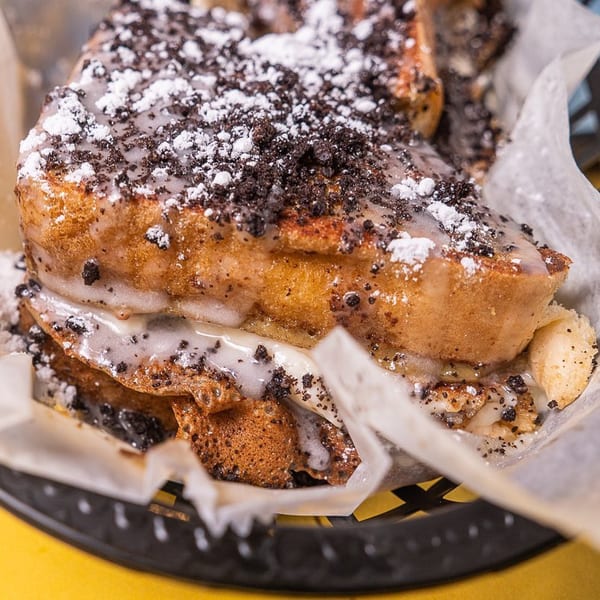 Stack House's French toast with white icing, powdered sugar, and cookie crumbles in a basket.