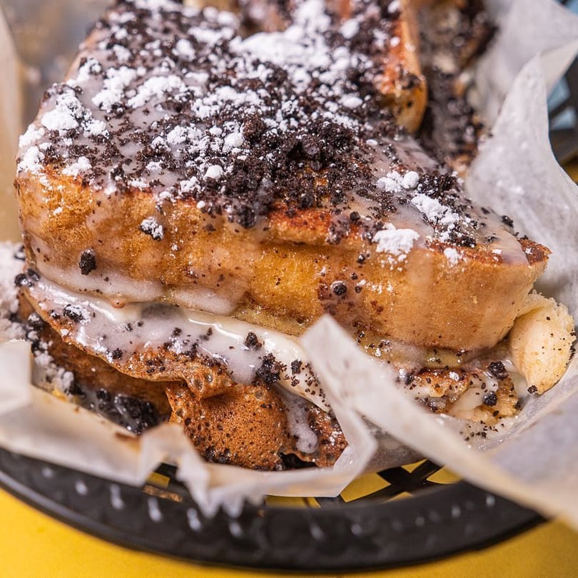 Stack House's French toast with white icing, powdered sugar, and cookie crumbles in a basket.