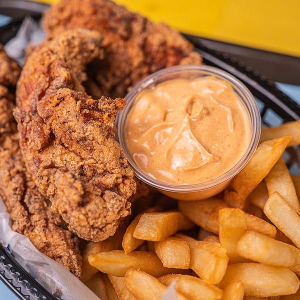 Crispy fried chicken tenders, golden french fries, and a cup of dipping sauce in a basket.