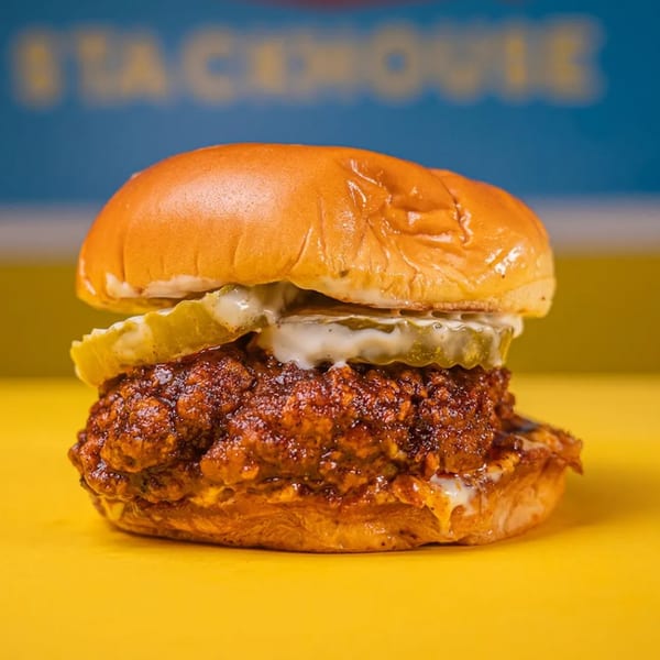 A Stack House southern fried chicken sandwich with pickles and sauce on a yellow surface.